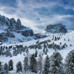 Panorama innevato delle Dolomiti, con valli e cime montuose illuminate dal sole in inverno.