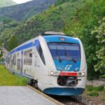 Treno panoramico che attraversa paesaggi mozzafiato in Italia, con montagne e vallate verdeggianti.
