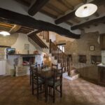 Interno accogliente di una casa di pietra con camino acceso e arredi rustici.